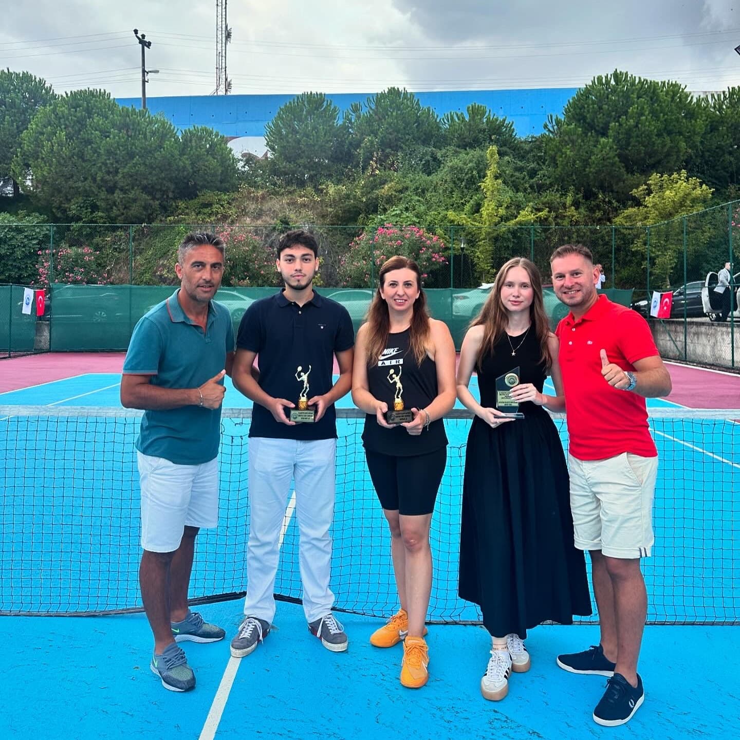 Mavi kortta ödüllerini tutan yetişkin sporcular ve kulüp antrenörleri