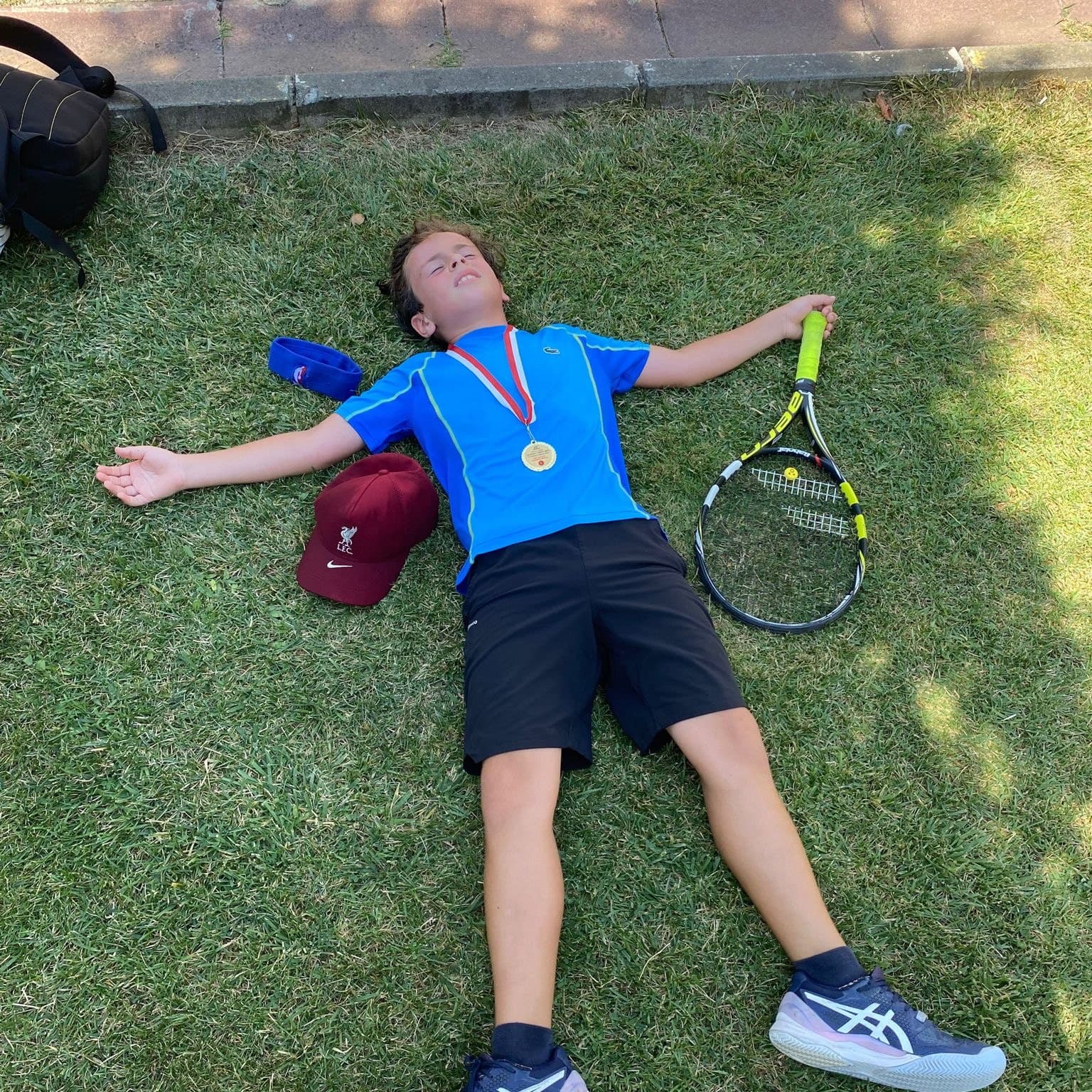 Maç sonrası madalyası ve raketiyle çimende sırtüstü dinlenen genç sporcu