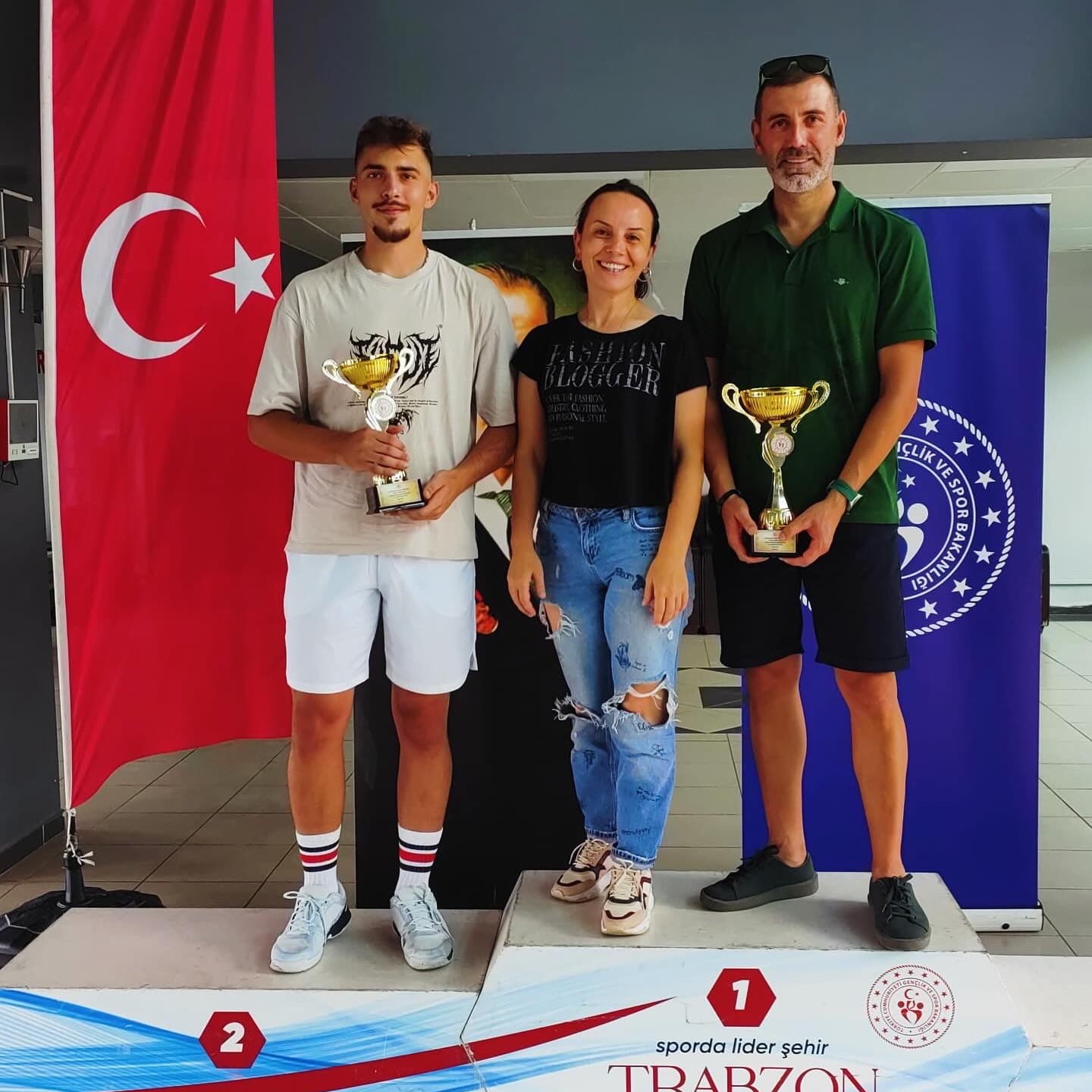 Turnuva ödül töreni podyumunda kupalarını tutan birinci ve ikinci sporcular